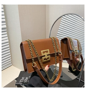 Detail of a brown glossy leather square bag with a chunky gold chain strap and buckle