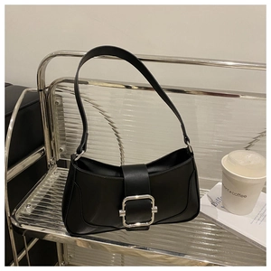 Detail of black glossy baguette bag with large silver buckle on a minimalist shelf