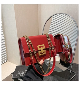 Detail of red patent leather handbag with gold chain strap and geometric buckle