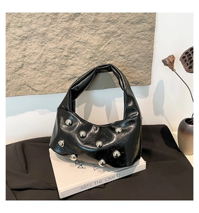 Detail of glossy black patent leather crescent bag with silver dome studs and wide strap