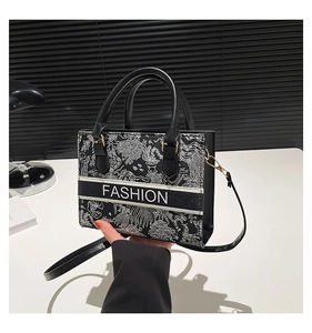 Detail showing the intricate white floral embroidery on a black textile crossbody bag