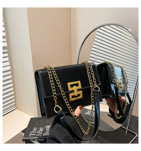 Close-up of black square flap bag with shiny finish and bold gold geometric buckle