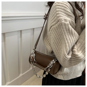 Detail view of a brown cylinder crossbody bag with silver chain and metal brand plaque