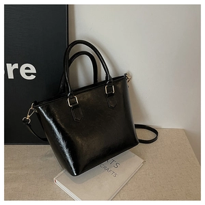 Détail d'un sac seau en cuir noir brillant avec des finitions dorées et bandoulière