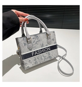 Detail of embroidered jacquard tote bag with FASHION logo and gray leather handles