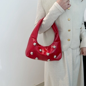Red patent leather crescent bag with silver stud accents worn by a model in a white suit
