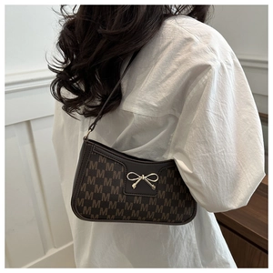 Close-up of brown crescent bag with M-pattern print and gold bow metal buckle