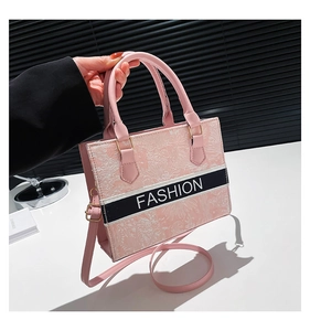 Detail of pink crossbody bag with floral embroidery and white Fashion lettering on band