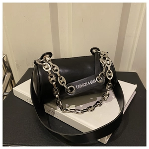 Detail of black cylinder bag with silver chunky chain and wide strap on white books