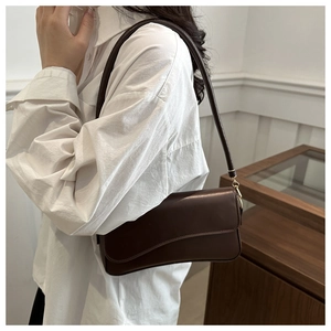 Macro view of minimalist brown leather shoulder bag with wavy flap and gold hardware