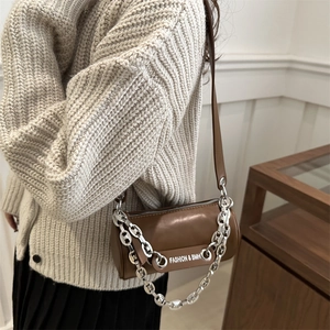 Brown cylinder crossbody bag with silver chain strap worn by model in casual style
