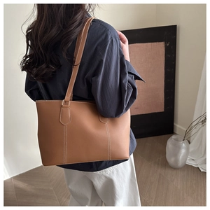 Detail view of brown leather tote bag with white contrast stitching and long shoulder straps