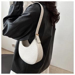 Detail of white crescent bag showing faux crocodile texture and gold hardware on shoulder strap