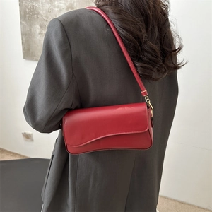 Modern red leather underarm bag with minimalist flap shown on model with dark blazer