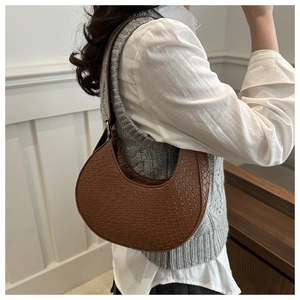 Detail shot of a brown crescent shoulder bag with woven texture on a white shirt model