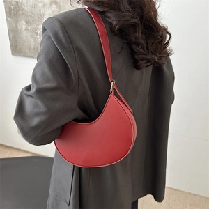 Red crescent leather shoulder bag shown on model in black suit for 2025 fashion trend