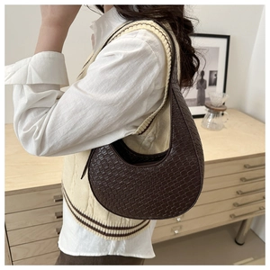 Detail of dark brown croc-embossed crescent shoulder bag on model in a cozy room