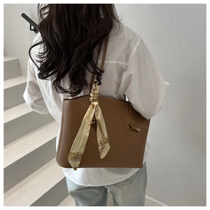 Dettaglio borsa tote in pelle marrone scuro con elegante foulard di seta sulla maniglia