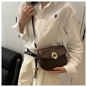 Detail of a dark brown leather saddle bag with a golden horseshoe lock and slim strap