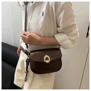 Detailed view of brown leather saddle bag with golden horseshoe buckle worn by model