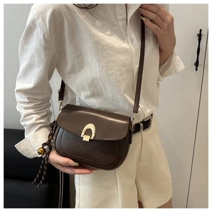 Detail of dark brown vintage saddle bag with gold horseshoe buckle and woven pendant