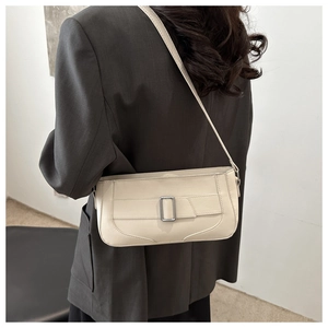Close-up of cream baguette bag with silver buckle worn over a grey oversized blazer