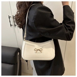 Détail du sac bandoulière blanc cassé avec boucle nœud doré sur veste noire