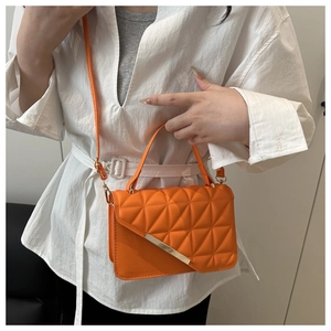 Close-up of orange quilted crossbody bag with gold metal buckle and leather handle