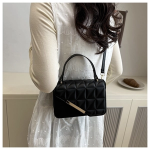 Detail of black quilted geometric texture handbag with elegant diagonal gold metal bar accent