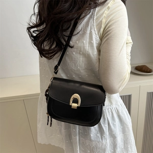 Chic black saddle bag with gold horseshoe clasp and woven charm worn by a model