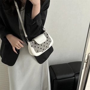 Sac bandoulière chic en cuir blanc à pois gris porté par un mannequin devant le miroir