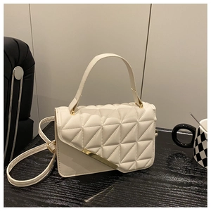 Close-up of beige quilted crossbody bag with golden hardware and top handle on dark table