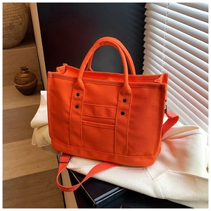 Detail view of bright orange canvas tote bag with black rivets and matching shoulder strap