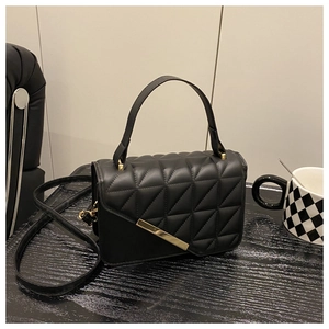 Detail of black quilted crossbody bag with gold metal trim and chain strap on dark surface