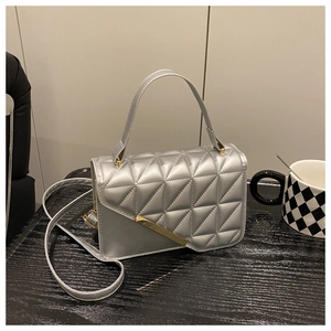 Detail showing silver quilted leather texture and slanted gold metal bar on the handbag