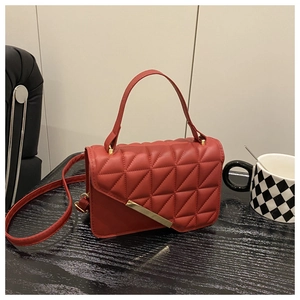Close-up of red quilted crossbody bag with gold metal clasp on a dark wooden table