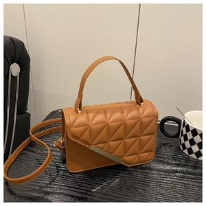 Detail of caramel brown quilted PU leather bag with gold metal trim on black wood table