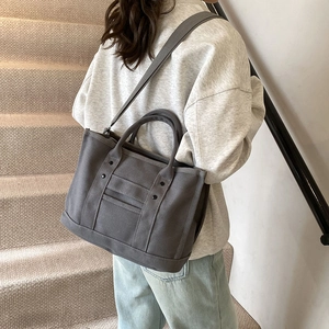 Dark grey canvas tote bag with decorative vertical straps and rivets on stairs