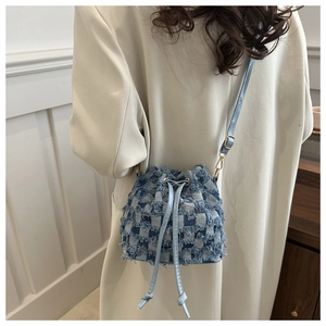 Detail of blue and white plaid denim bucket bag with frayed edges and drawstring closure