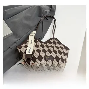 Detail of argyle pattern tote bag with leather logo tag and decorative strap