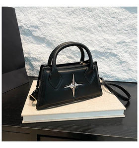 Detailaufnahme der schwarzen Leder-Trapeztasche mit silbernem Stern auf strukturiertem Fels