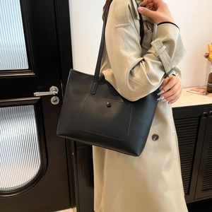 Minimalist black leather tote bag with crossbody strap shown in a modern lifestyle setting