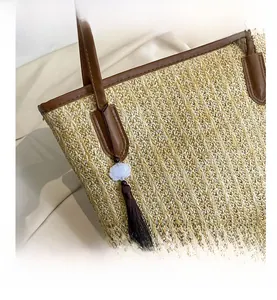 Detail of straw tote bag showing brown leather trim and stylish tassel pendant