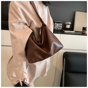 Macro view of textured vintage brown leather tote showing soft pleats and wide strap