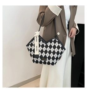 Detail of checkered tote bag with V-cut top and decorative brand strap hanging on the side