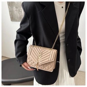 Detail view of apricot quilted crossbody bag with gold chain strap and metal tassels