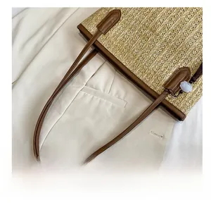 Detail of straw woven tote bag showing brown leather handles and decorative tassel