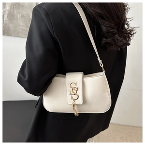 Detail of cream shoulder bag with golden S-buckle and tassel on black blazer outfit
