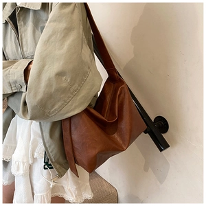 Detail view of a large brown leather tote bag with wide strap on a model with olive jacket