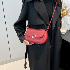 Red leather saddle shoulder bag with unique metal buckle on a black coat model